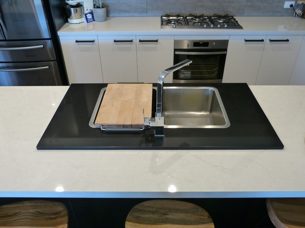 This is an example of a large contemporary galley open plan kitchen in Adelaide with a double-bowl sink, flat-panel cabinets, black cabinets, laminate benchtops, grey splashback, cement tile splashback, stainless steel appliances, laminate floors, with island, brown floor and white benchtop.