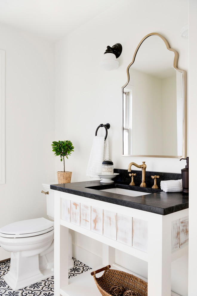 Country powder room in Minneapolis with open cabinets, distressed cabinets, white walls, an undermount sink, multi-coloured floor and black benchtops.