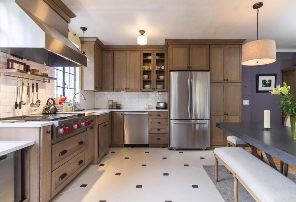 Inspiration for a transitional l-shaped porcelain tile and white floor eat-in kitchen remodel in Portland with an undermount sink, shaker cabinets, solid surface countertops, white backsplash, ceramic backsplash, stainless steel appliances, an island, white countertops and medium tone wood cabinets