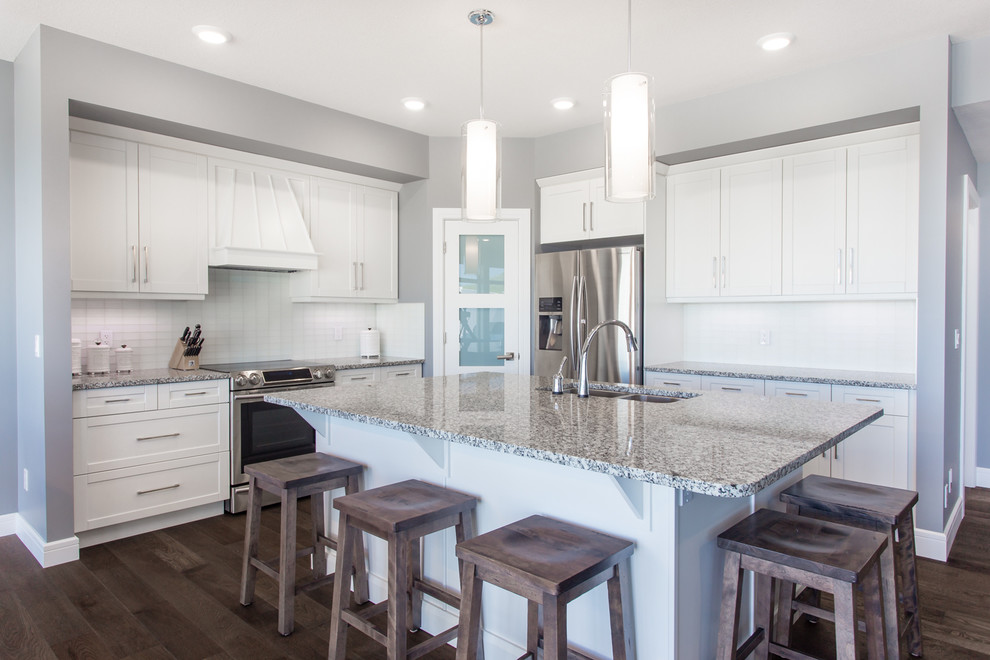 This is an example of a mid-sized contemporary l-shaped eat-in kitchen in Calgary with an undermount sink, shaker cabinets, white cabinets, granite benchtops, white splashback, glass sheet splashback, stainless steel appliances, medium hardwood floors and with island.