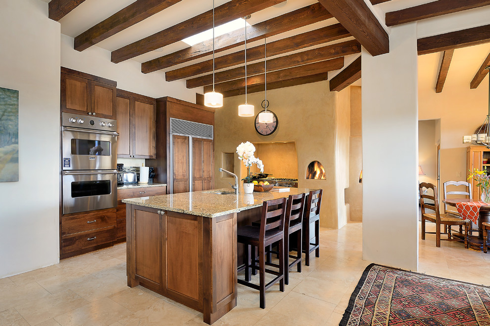 Photo of a l-shaped open plan kitchen in Albuquerque with an undermount sink, shaker cabinets, dark wood cabinets, granite benchtops, beige splashback, travertine floors, with island, beige floor and panelled appliances.