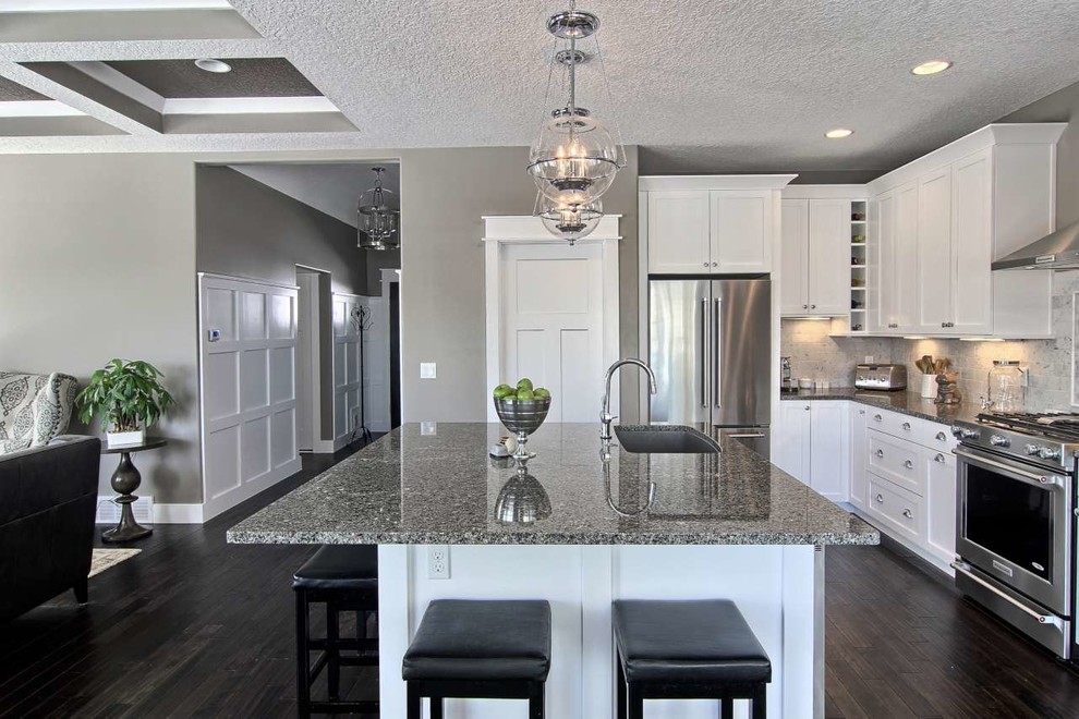 Mid-sized transitional l-shaped dark wood floor open concept kitchen photo with a single-bowl sink, shaker cabinets, white cabinets, granite countertops, gray backsplash, stone tile backsplash, stainless steel appliances and an island