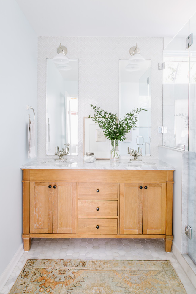 This is an example of a mid-sized eclectic master bathroom in Austin with furniture-like cabinets, light wood cabinets, a corner shower, a two-piece toilet, white tile, glass sheet wall, blue walls, marble floors, an undermount sink, marble benchtops, grey floor and a shower curtain.