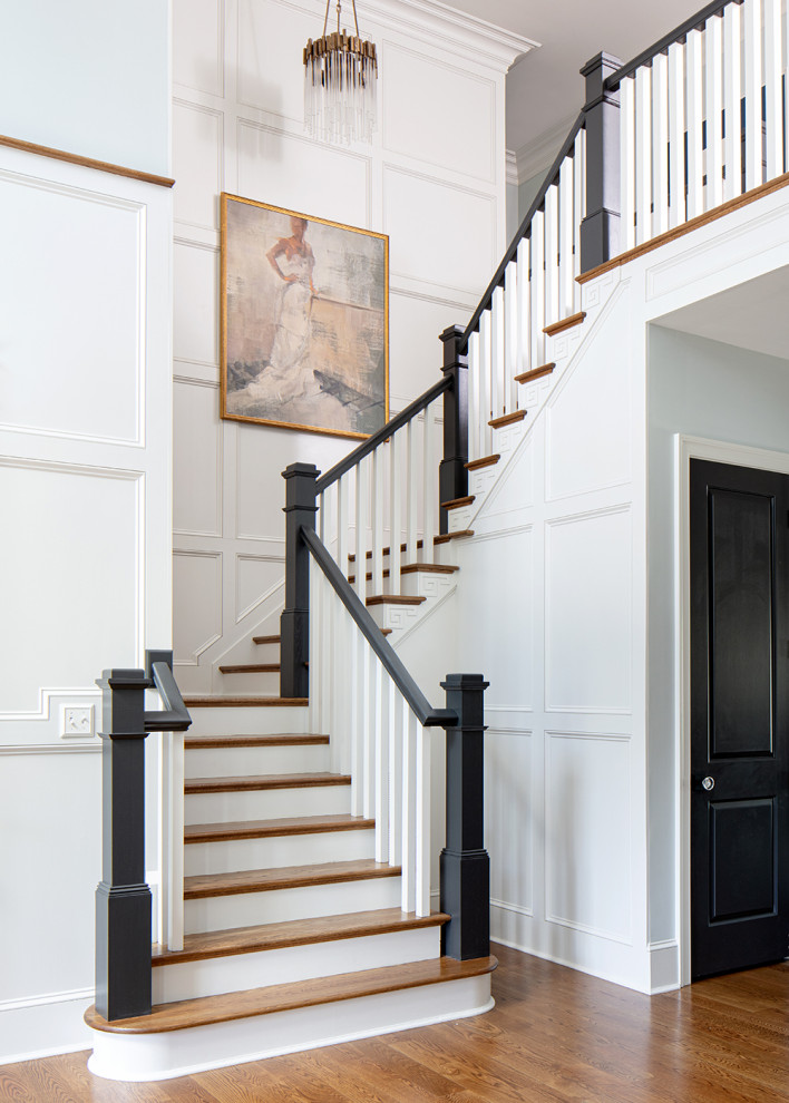 На фото: большая п-образная лестница в классическом стиле с деревянными ступенями, крашенными деревянными подступенками, деревянными перилами и панелями на стенах