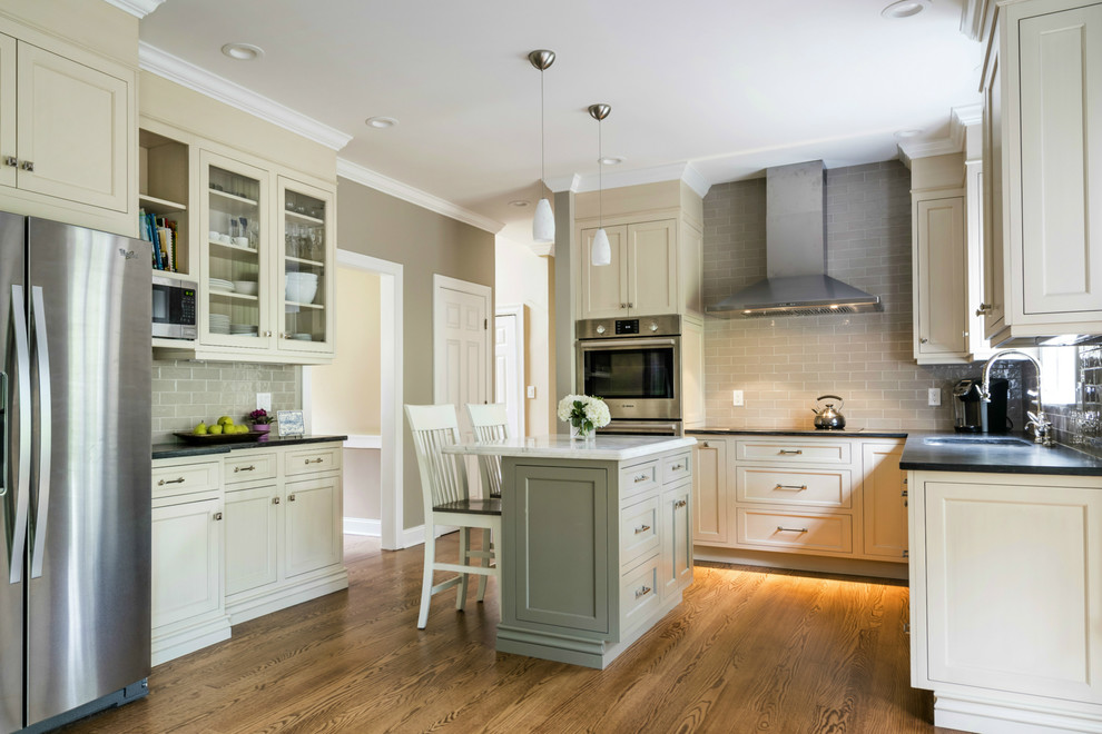 Small transitional u-shaped medium tone wood floor and brown floor open concept kitchen photo with an undermount sink, beaded inset cabinets, beige cabinets, gray backsplash, ceramic backsplash, stainless steel appliances, an island and limestone countertops