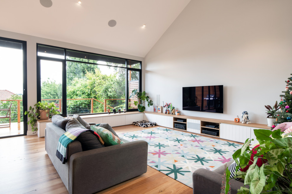Photo of a contemporary living room in Sydney with grey walls, medium hardwood floors, a wall-mounted tv, brown floor and vaulted.