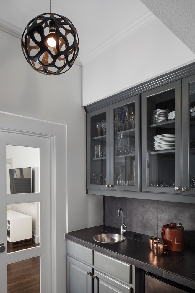 Inspiration for a mid-sized transitional single-wall wet bar in Austin with a drop-in sink, raised-panel cabinets, grey cabinets, tile benchtops, grey splashback, cement tile splashback and dark hardwood floors.