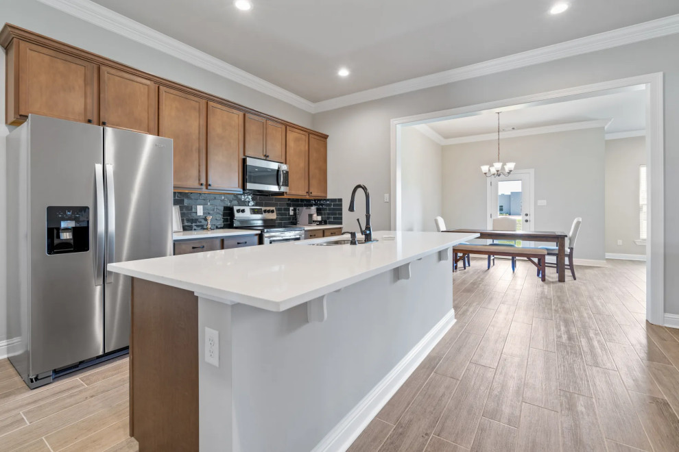 Mid-sized elegant single-wall ceramic tile and brown floor enclosed kitchen photo in Houston with an undermount sink, brown cabinets, black backsplash, stainless steel appliances, an island and white countertops