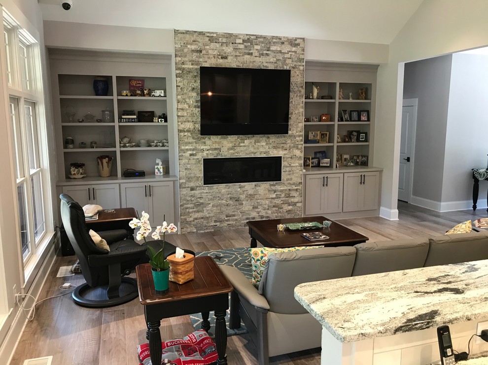 Photo of a mid-sized arts and crafts open concept living room in Raleigh with white walls, light hardwood floors, a ribbon fireplace, a stone fireplace surround, a wall-mounted tv and brown floor.