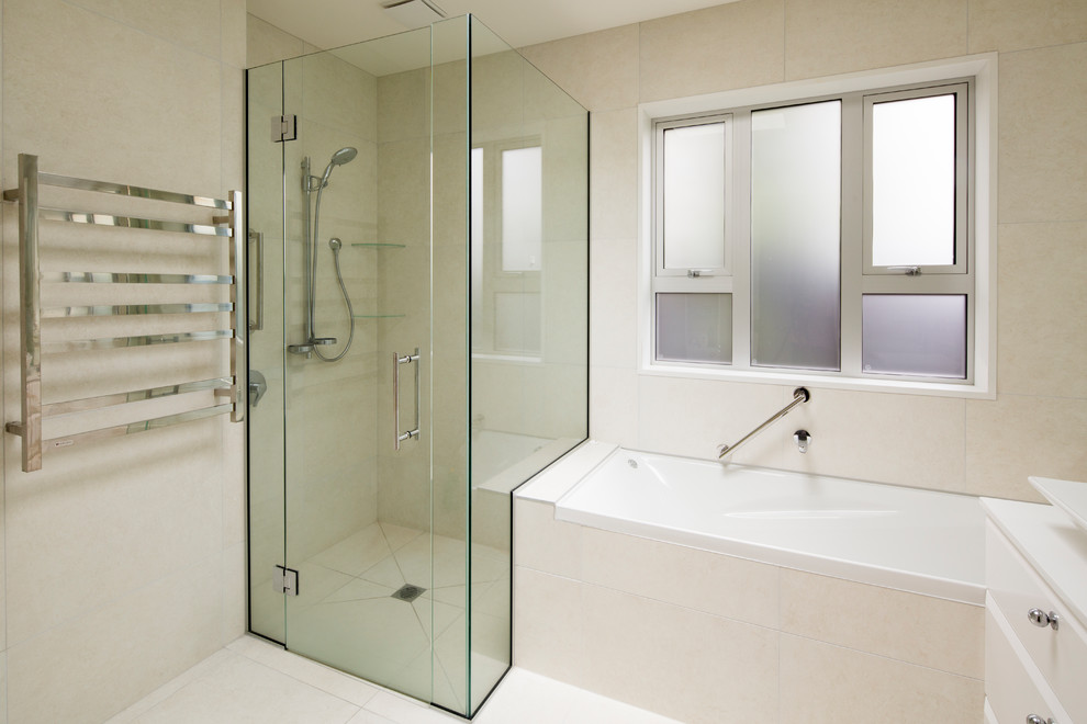 This is an example of a mid-sized traditional master bathroom in Christchurch with a drop-in tub, an alcove shower, a one-piece toilet, beige tile, porcelain tile, beige walls, porcelain floors, beige floor and a hinged shower door.