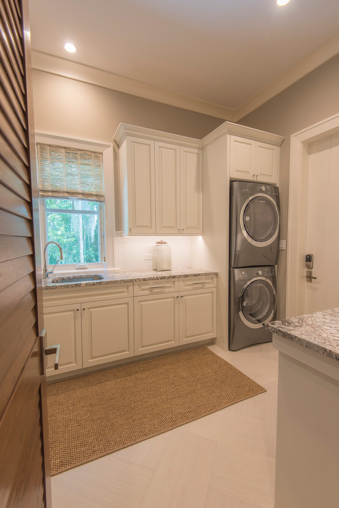 Design ideas for a large tropical galley dedicated laundry room in Tampa with an undermount sink, raised-panel cabinets, white cabinets, granite benchtops, ceramic floors, a stacked washer and dryer and grey walls.