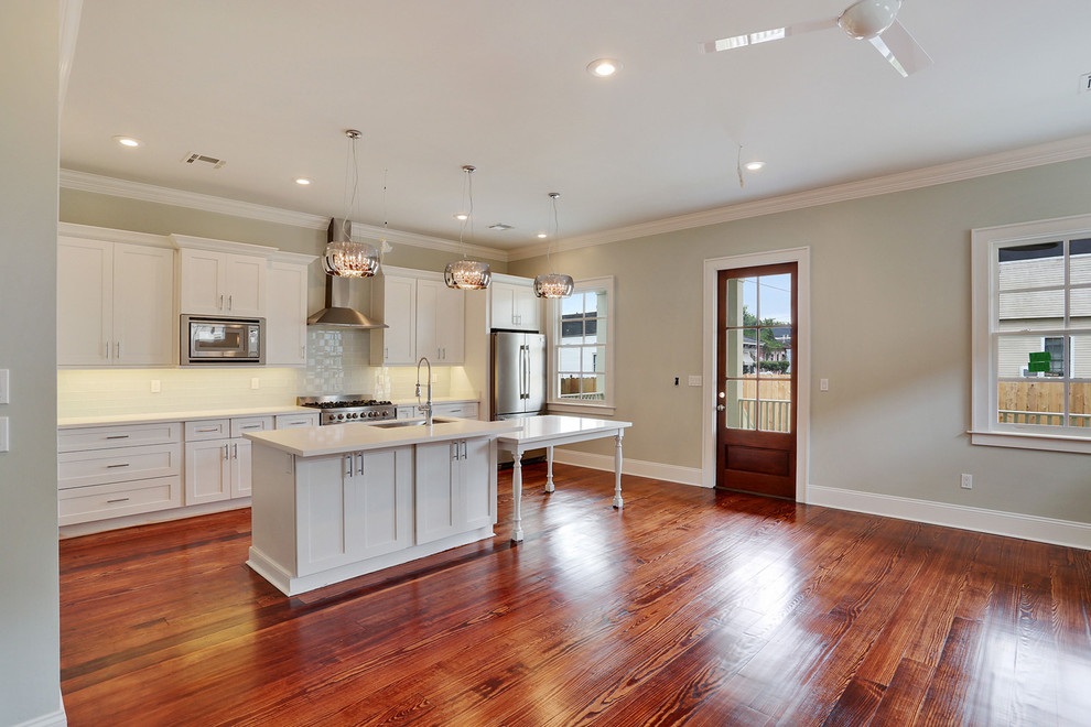 Mid-sized traditional single-wall open plan kitchen in New Orleans with an undermount sink, recessed-panel cabinets, white cabinets, quartz benchtops, white splashback, glass tile splashback, stainless steel appliances, medium hardwood floors and with island.