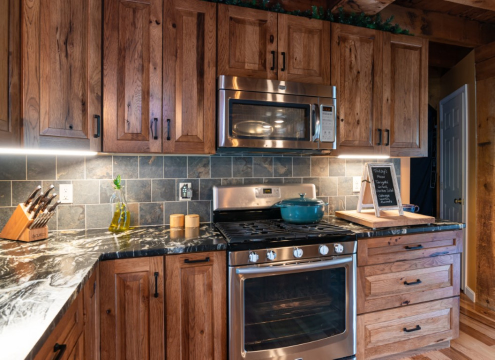 Example of a mountain style l-shaped medium tone wood floor kitchen design in Boston with an undermount sink, raised-panel cabinets, medium tone wood cabinets, granite countertops, gray backsplash, stainless steel appliances, an island and black countertops