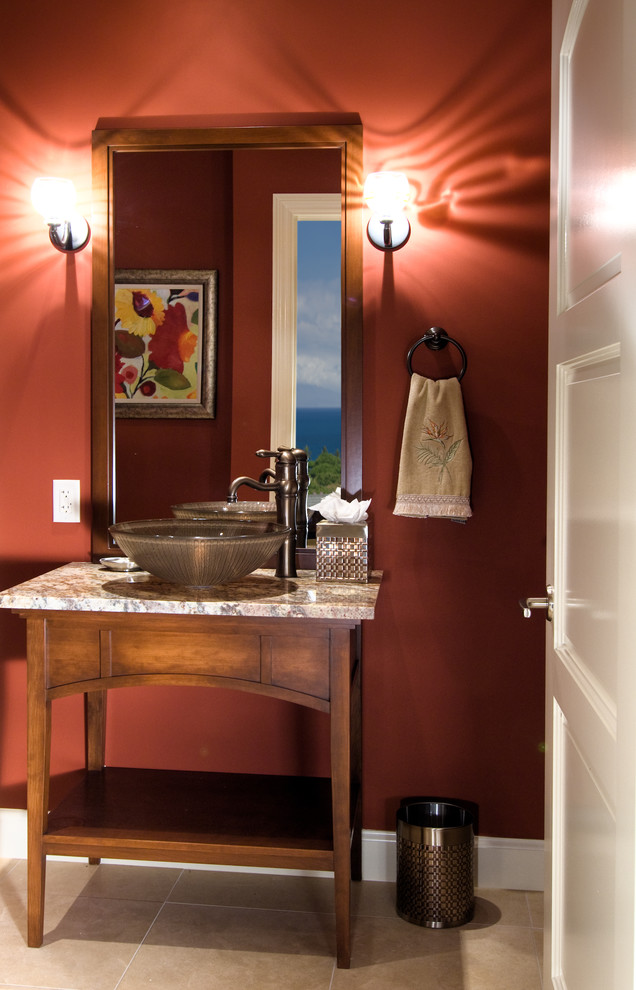 Tropical bathroom in Hawaii with furniture-like cabinets, medium wood cabinets, a one-piece toilet, beige tile, stone tile, red walls, limestone floors, a vessel sink and granite benchtops.