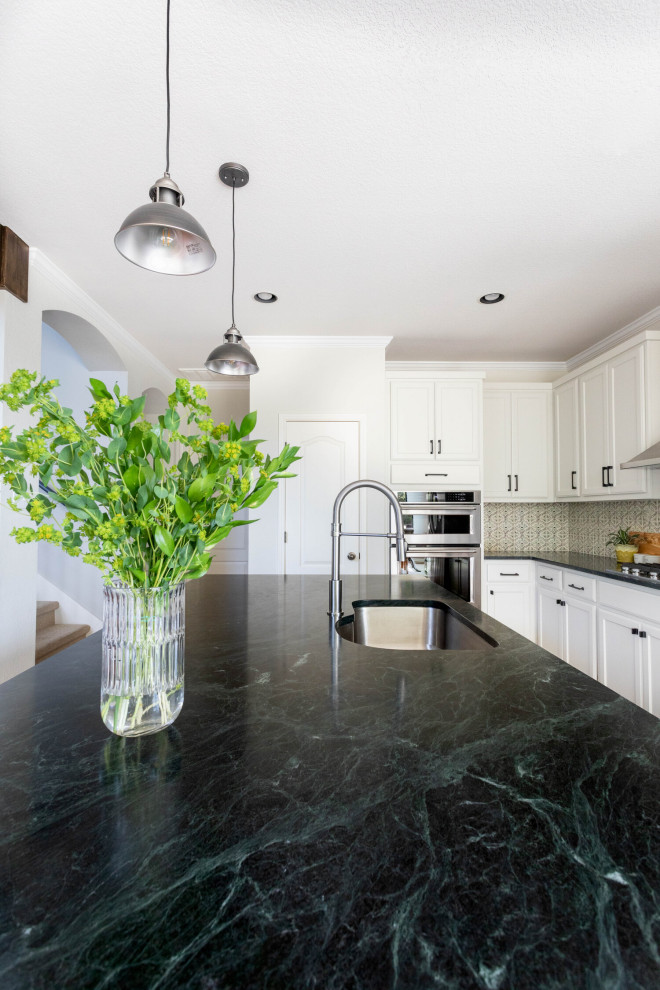 Mid-sized transitional l-shaped medium tone wood floor and brown floor eat-in kitchen photo in Austin with an undermount sink, shaker cabinets, white cabinets, soapstone countertops, beige backsplash, ceramic backsplash, stainless steel appliances, an island and black countertops