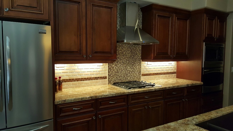 Example of a transitional single-wall eat-in kitchen design in Phoenix with an undermount sink, dark wood cabinets, granite countertops, brown backsplash, glass tile backsplash, stainless steel appliances and an island