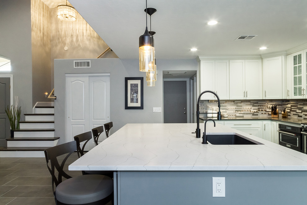 Open concept kitchen - mid-sized transitional l-shaped porcelain tile and gray floor open concept kitchen idea in Phoenix with an undermount sink, shaker cabinets, white cabinets, quartz countertops, gray backsplash, glass tile backsplash, black appliances, an island and gray countertops