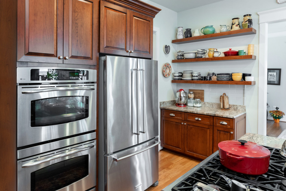Inspiration for a mid-sized traditional l-shaped kitchen in DC Metro with an undermount sink, raised-panel cabinets, dark wood cabinets, granite benchtops, grey splashback, ceramic splashback, stainless steel appliances, medium hardwood floors, with island, brown floor and grey benchtop.