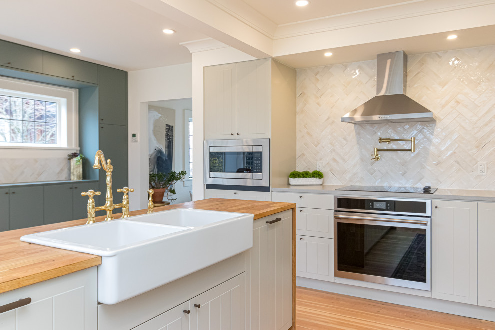 Example of a mid-sized transitional l-shaped medium tone wood floor, brown floor and coffered ceiling eat-in kitchen design with a farmhouse sink, raised-panel cabinets, gray cabinets, wood countertops, beige backsplash, ceramic backsplash, stainless steel appliances, an island and brown countertops