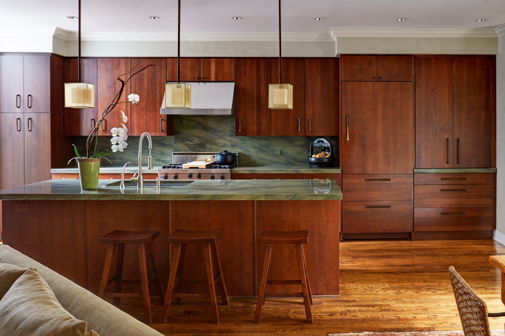 Photo of an asian galley kitchen in Chicago with an undermount sink, flat-panel cabinets, dark wood cabinets, green splashback, panelled appliances, medium hardwood floors, with island, brown floor and green benchtop.