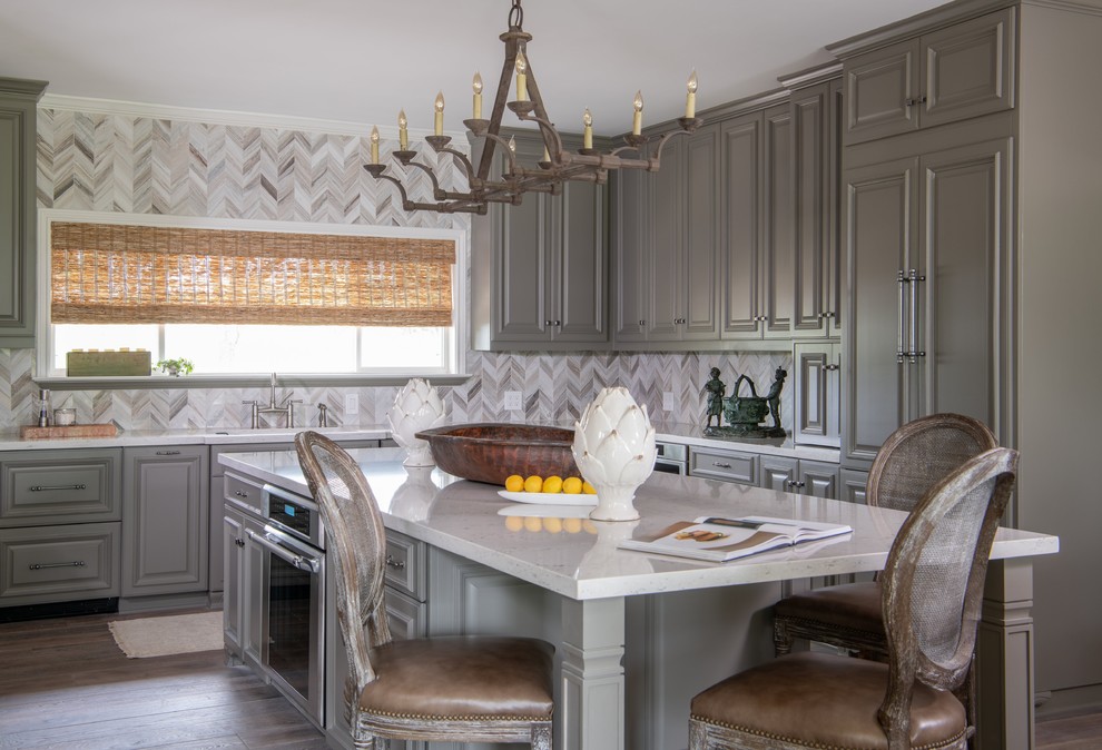 Inspiration for a traditional l-shaped eat-in kitchen in Austin with an undermount sink, raised-panel cabinets, grey cabinets, beige splashback, mosaic tile splashback, panelled appliances, medium hardwood floors, with island, brown floor and white benchtop.