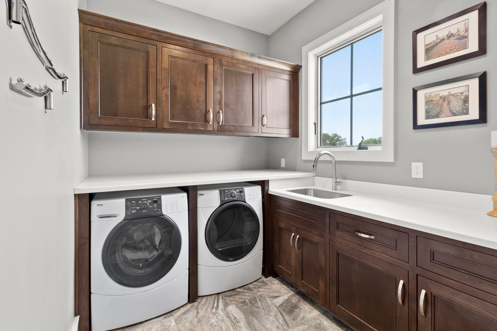 Large transitional l-shaped dedicated laundry room in Kansas City with a single-bowl sink, dark wood cabinets, quartz benchtops, grey walls, ceramic floors, a side-by-side washer and dryer, multi-coloured floor, white benchtop and recessed-panel cabinets.