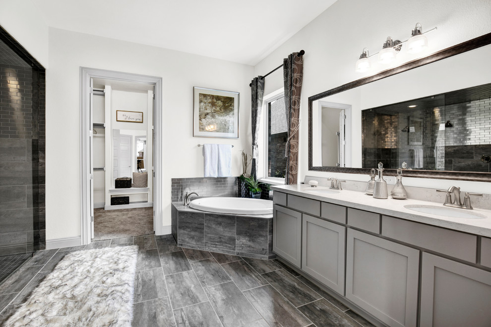 This is an example of a large contemporary master bathroom in Dallas with recessed-panel cabinets, grey cabinets, a corner tub, an alcove shower, gray tile, stone tile, white walls, porcelain floors, an undermount sink, solid surface benchtops, grey floor and a sliding shower screen.