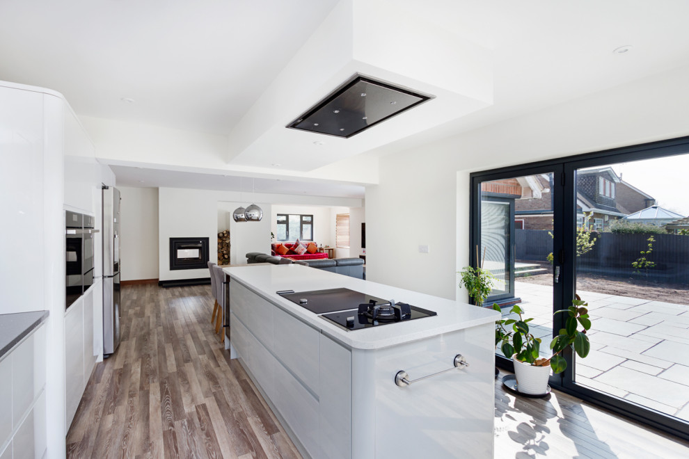 Inspiration for a mid-sized contemporary l-shaped open plan kitchen in West Midlands with a drop-in sink, flat-panel cabinets, white cabinets, grey splashback, panelled appliances, laminate floors, with island, grey floor and grey benchtop.