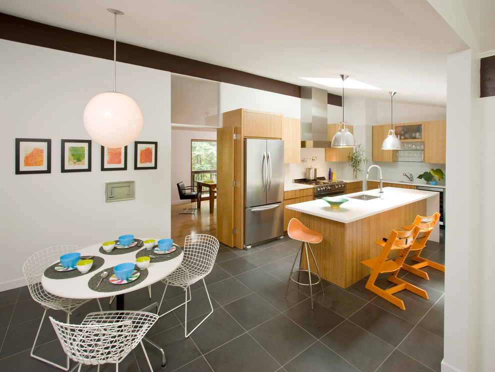 Mid-sized midcentury l-shaped eat-in kitchen in New York with an undermount sink, flat-panel cabinets, light wood cabinets, solid surface benchtops, white splashback, ceramic splashback, stainless steel appliances, slate floors, with island, grey floor and white benchtop.