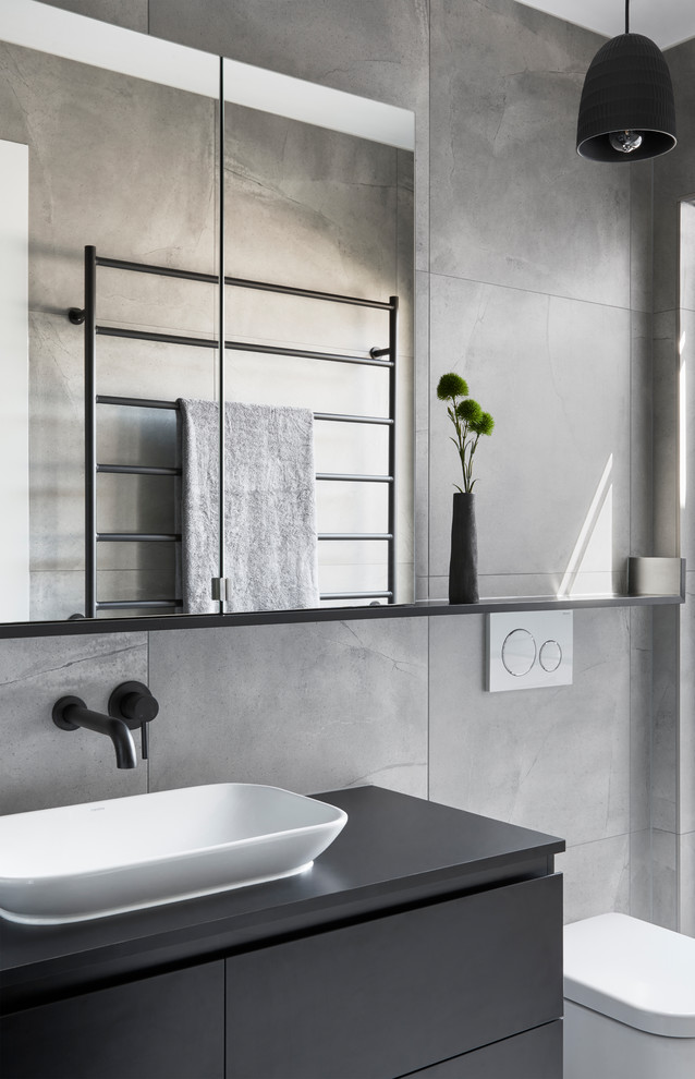 This is an example of a small modern 3/4 bathroom in Melbourne with black cabinets, a curbless shower, gray tile, porcelain tile, grey walls, porcelain floors, laminate benchtops, grey floor, a hinged shower door and black benchtops.