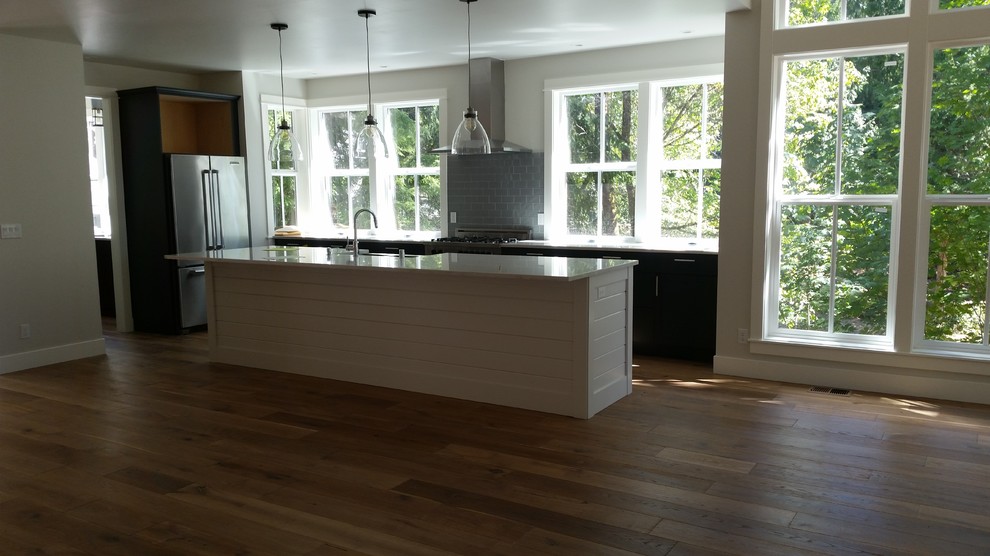 Photo of a large modern l-shaped open plan kitchen in Seattle with a farmhouse sink, flat-panel cabinets, dark wood cabinets, quartzite benchtops, grey splashback, glass tile splashback, stainless steel appliances, dark hardwood floors, with island, brown floor and white benchtop.