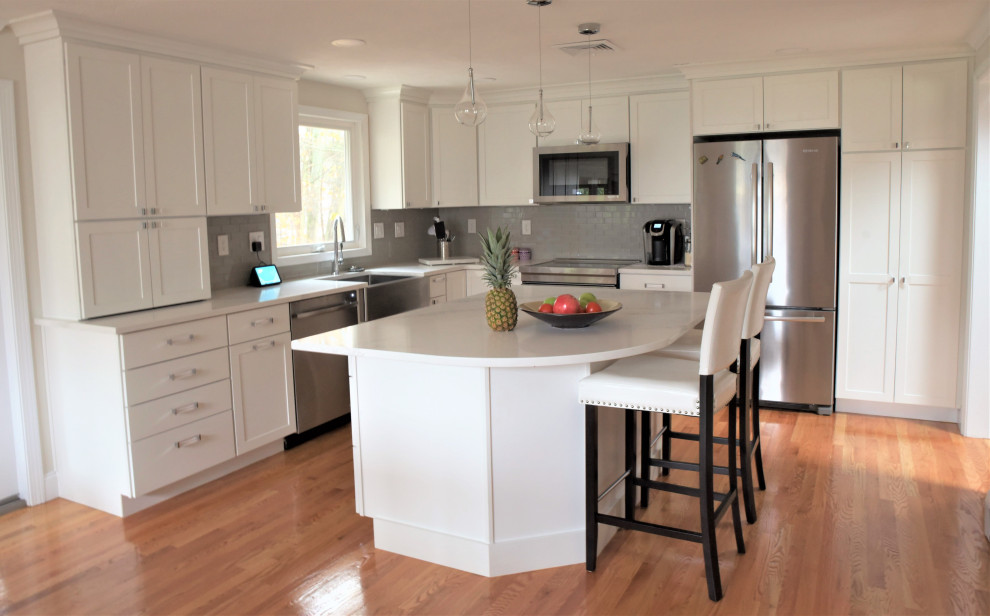 Mid-sized transitional l-shaped light wood floor and brown floor eat-in kitchen photo in Boston with a farmhouse sink, shaker cabinets, white cabinets, quartz countertops, gray backsplash, ceramic backsplash, stainless steel appliances, an island and white countertops