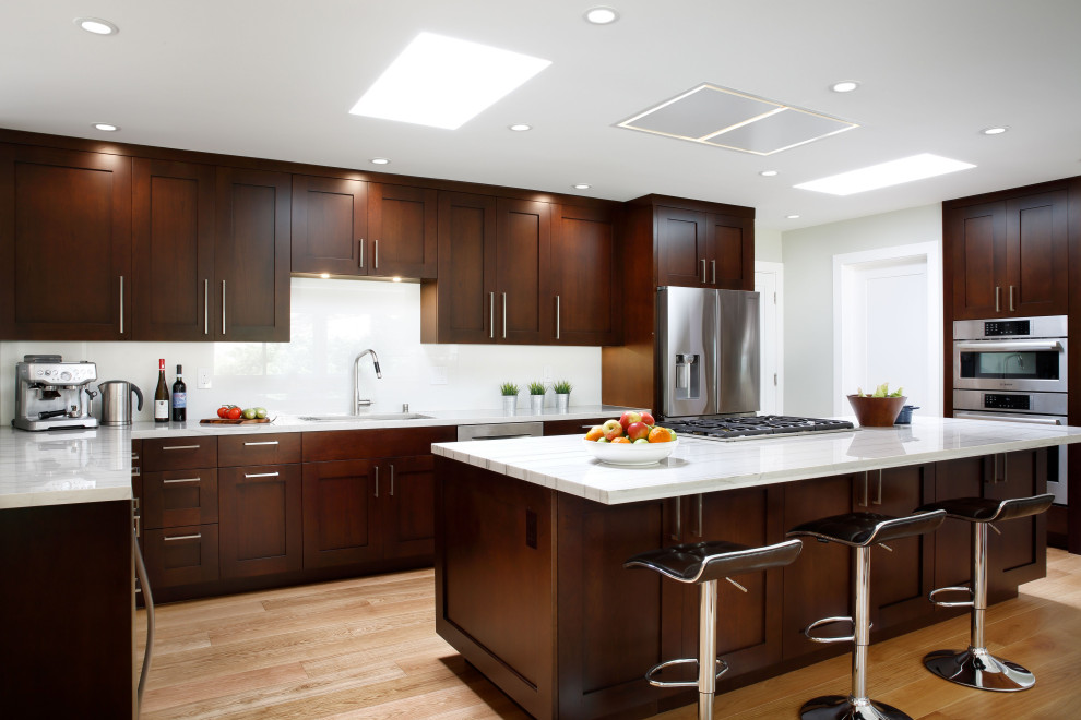 Inspiration for a large contemporary l-shaped open plan kitchen in San Francisco with an undermount sink, shaker cabinets, medium wood cabinets, quartzite benchtops, white splashback, porcelain splashback, stainless steel appliances, light hardwood floors, with island and white benchtop.