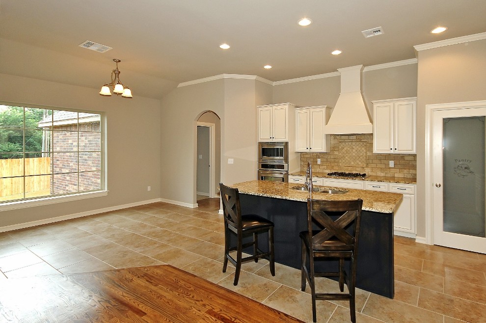 Open concept kitchen - large transitional galley ceramic tile open concept kitchen idea with a double-bowl sink, raised-panel cabinets, white cabinets, granite countertops, beige backsplash, stone tile backsplash, stainless steel appliances and an island