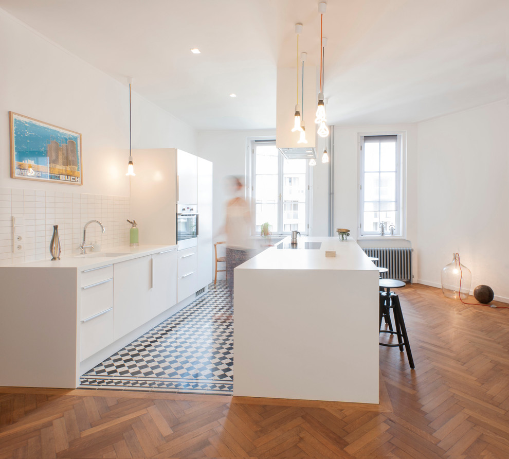 Design ideas for a large contemporary single-wall eat-in kitchen in Munich with flat-panel cabinets, white cabinets, white splashback, medium hardwood floors, with island, an undermount sink, ceramic splashback and panelled appliances.