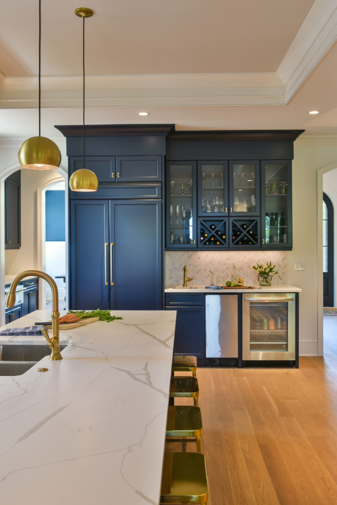 This is an example of a beach style wet bar in Charleston with blue cabinets, quartz benchtops, grey splashback, light hardwood floors and white benchtop.