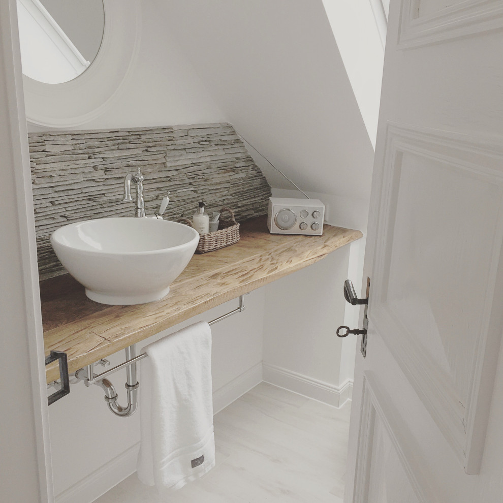 Inspiration for a small farmhouse cloakroom in Other with white cabinets, a two-piece toilet, white tiles, metro tiles, white walls, wood-effect flooring, a vessel sink, wooden worktops, grey floors and brown worktops.
