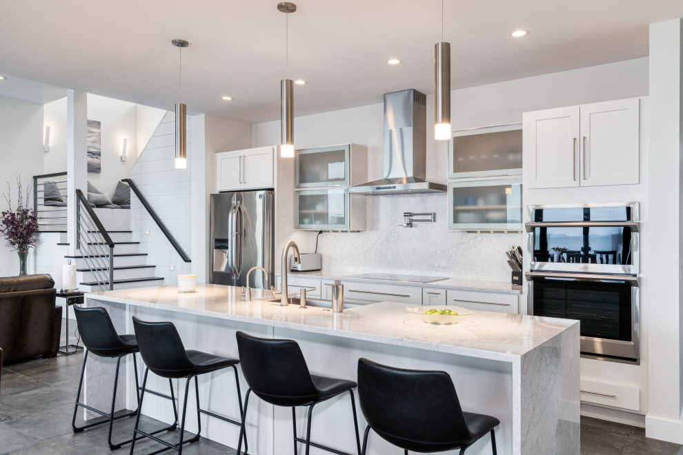 Mid-sized transitional single-wall open plan kitchen in New York with a farmhouse sink, shaker cabinets, white cabinets, quartz benchtops, white splashback, engineered quartz splashback, stainless steel appliances, vinyl floors, with island, grey floor and white benchtop.