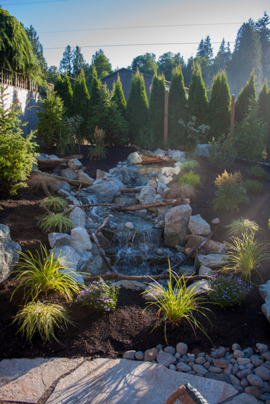 Photo of a mid-sized rustic full sun backyard stone water fountain landscape in Seattle for spring.