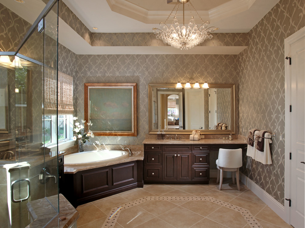 Example of a large transitional master travertine floor and beige floor drop-in bathtub design in Miami with raised-panel cabinets, dark wood cabinets, beige walls, an undermount sink, granite countertops, a two-piece toilet, a hinged shower door and beige countertops