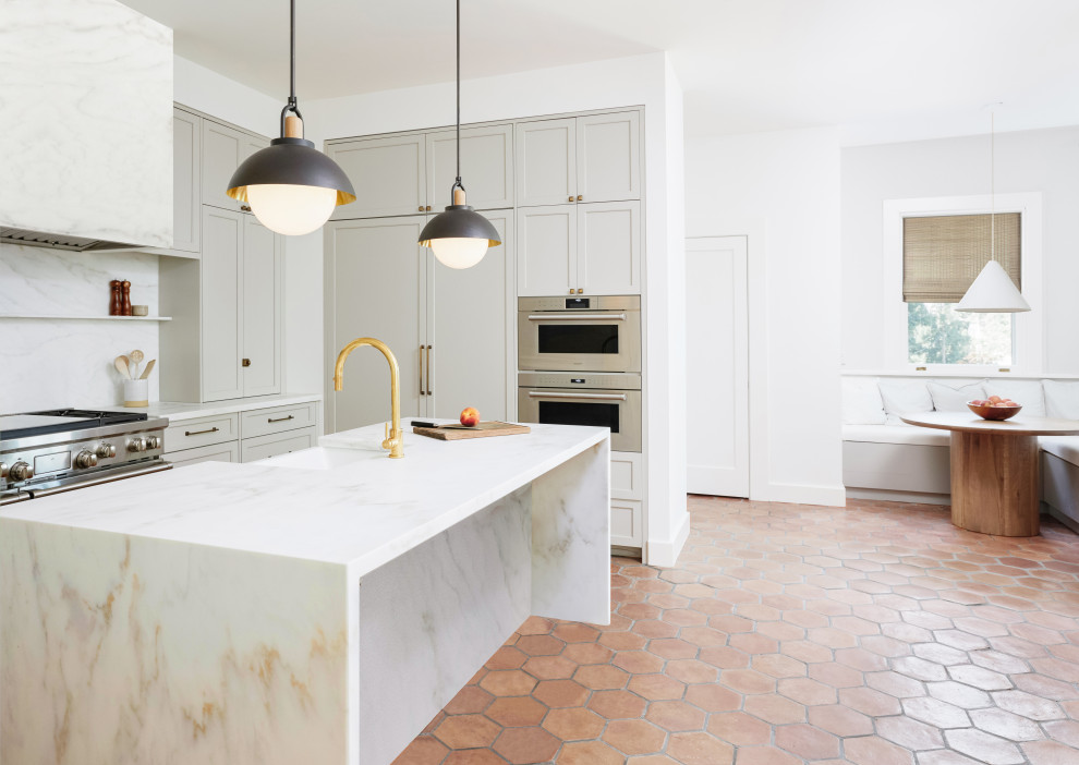 Inredning av ett klassiskt avskilt, mellanstort vit vitt l-kök, med en rustik diskho, skåp i shakerstil, grå skåp, marmorbänkskiva, vitt stänkskydd, stänkskydd i marmor, rostfria vitvaror, klinkergolv i terrakotta, en köksö och brunt golv