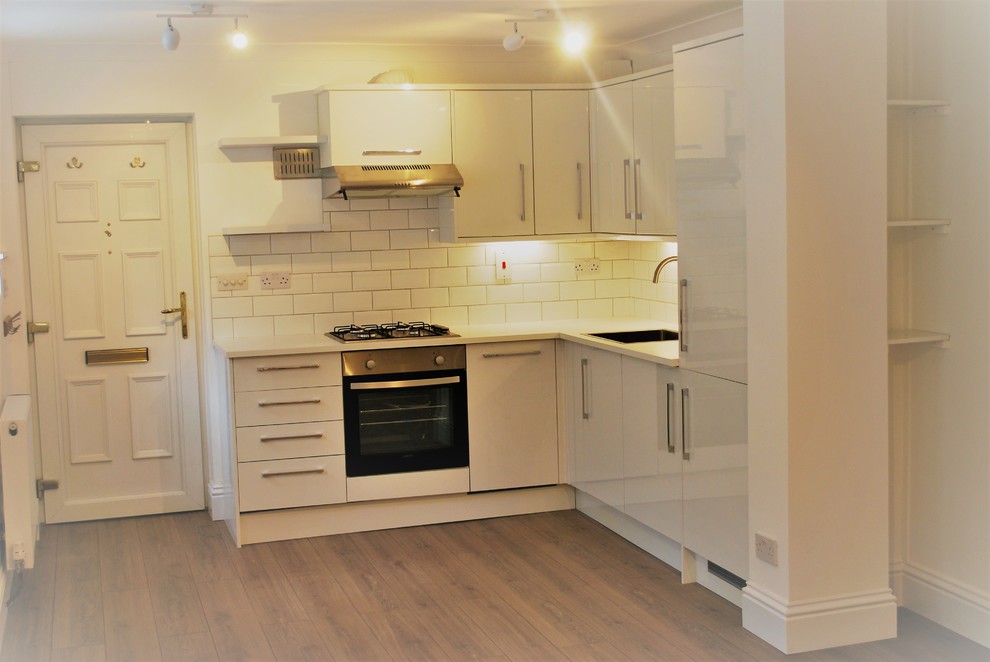 Small contemporary l-shaped eat-in kitchen in London with a single-bowl sink, flat-panel cabinets, white cabinets, laminate benchtops, white splashback, subway tile splashback, stainless steel appliances and laminate floors.