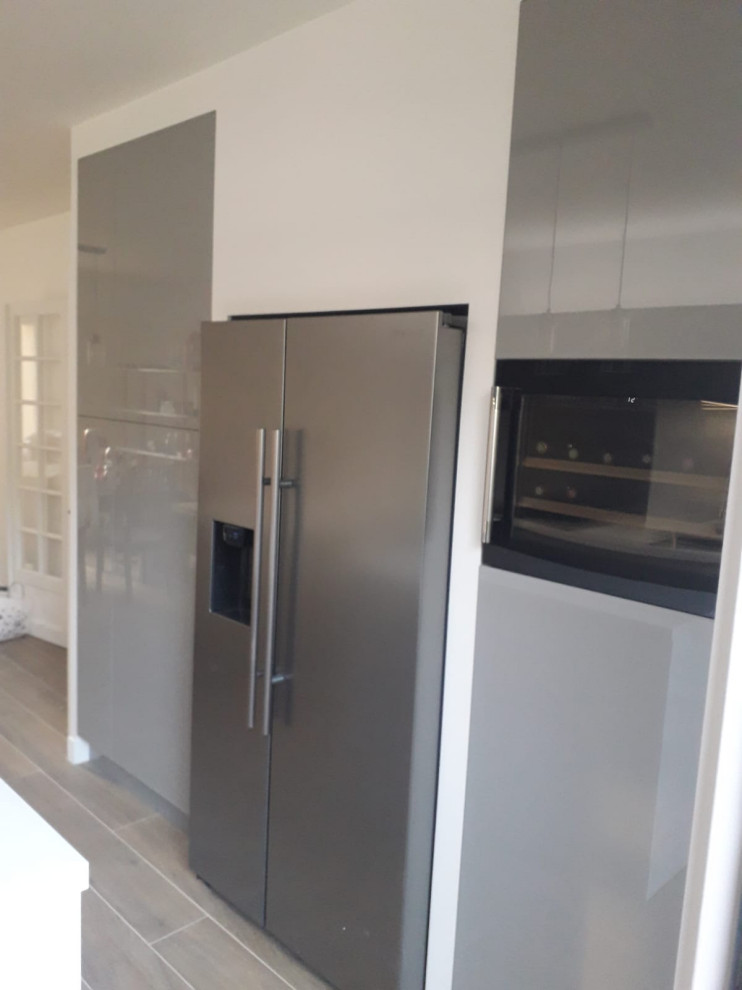 Large contemporary l-shaped eat-in kitchen in Paris with an integrated sink, recessed-panel cabinets, grey cabinets, wood benchtops, grey splashback, metal splashback, panelled appliances, laminate floors, with island, grey floor and white benchtop.