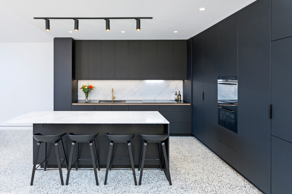 Mid-sized contemporary l-shaped open plan kitchen in Melbourne with flat-panel cabinets, black cabinets, marble benchtops, marble splashback, black appliances, concrete floors and with island.