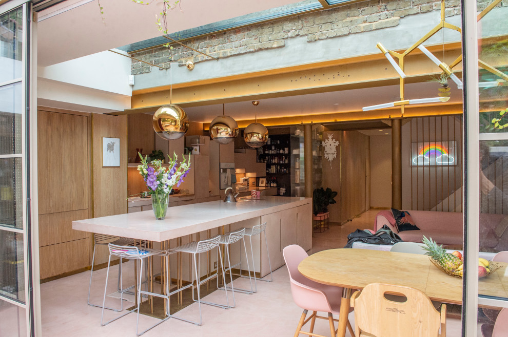 Large galley kitchen in London with an integrated sink, flat-panel cabinets, pink cabinets, concrete benchtops, yellow splashback, panelled appliances, concrete floors, with island, pink floor and pink benchtop.