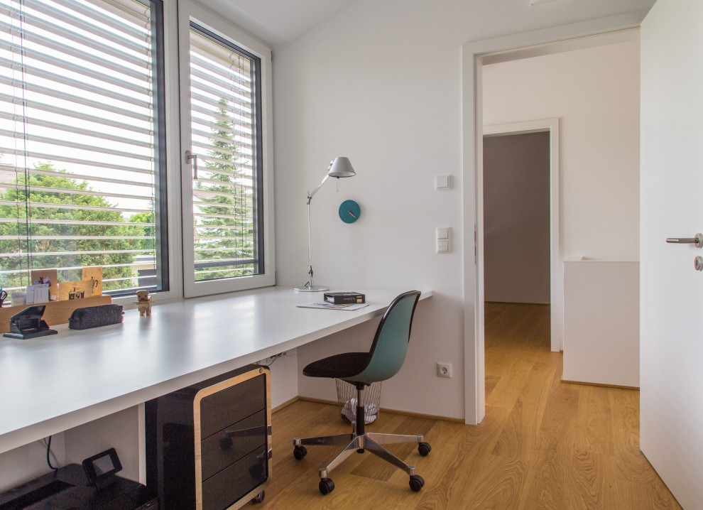 Modernes Arbeitszimmer mit weißer Wandfarbe und braunem Holzboden in München