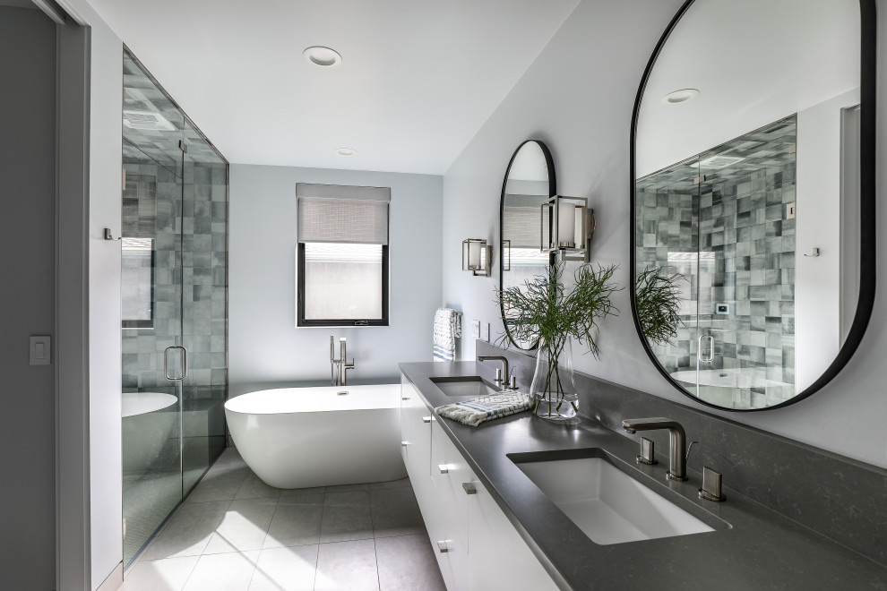Foto på ett funkis grå en-suite badrum, med släta luckor, vita skåp, ett fristående badkar, en dusch i en alkov, grå kakel, vit kakel, vita väggar, ett undermonterad handfat, bänkskiva i kvarts, grått golv och dusch med gångjärnsdörr