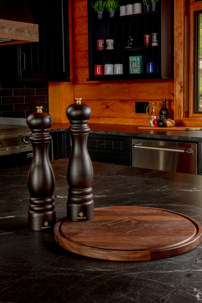 Example of a mid-sized mountain style l-shaped medium tone wood floor and brown floor eat-in kitchen design with a farmhouse sink, shaker cabinets, black cabinets, quartz countertops, black backsplash, stainless steel appliances, an island and black countertops