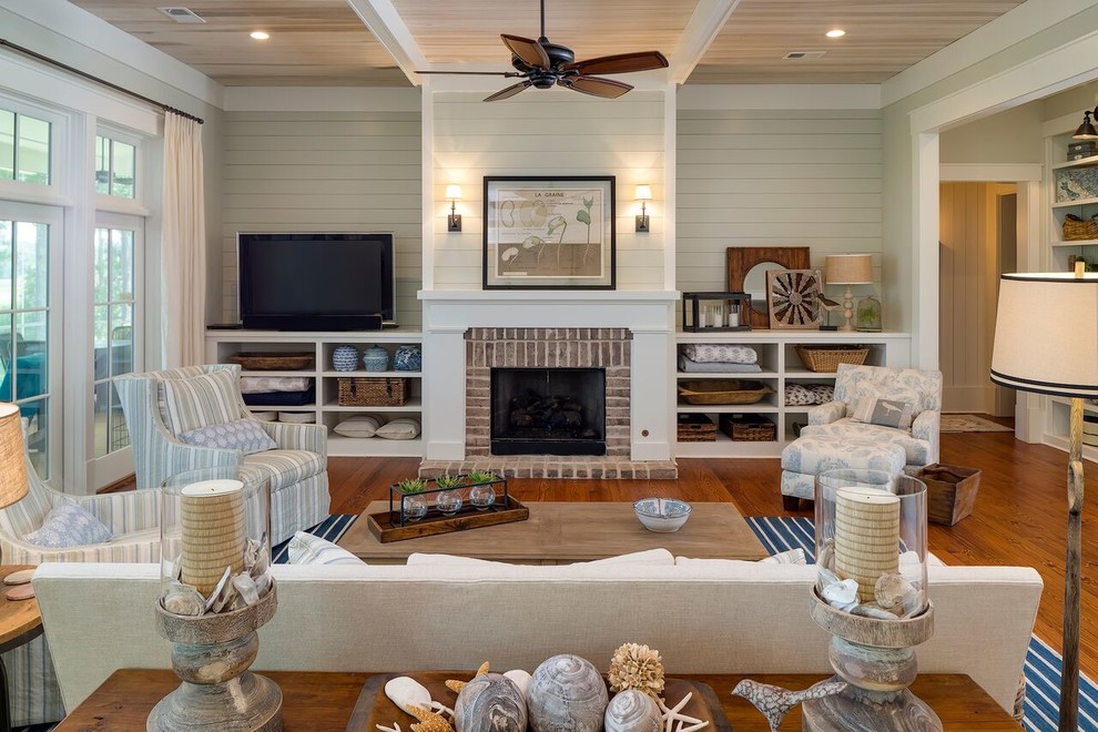 This is an example of a large beach style enclosed living room in Atlanta with beige walls, medium hardwood floors, a standard fireplace, a brick fireplace surround and a freestanding tv.