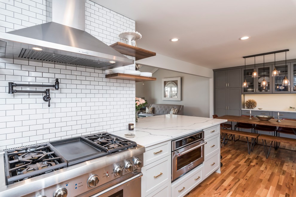 Example of a mid-sized transitional galley medium tone wood floor eat-in kitchen design in Denver with a farmhouse sink, shaker cabinets, gray cabinets, quartz countertops, white backsplash, porcelain backsplash, stainless steel appliances, a peninsula and white countertops